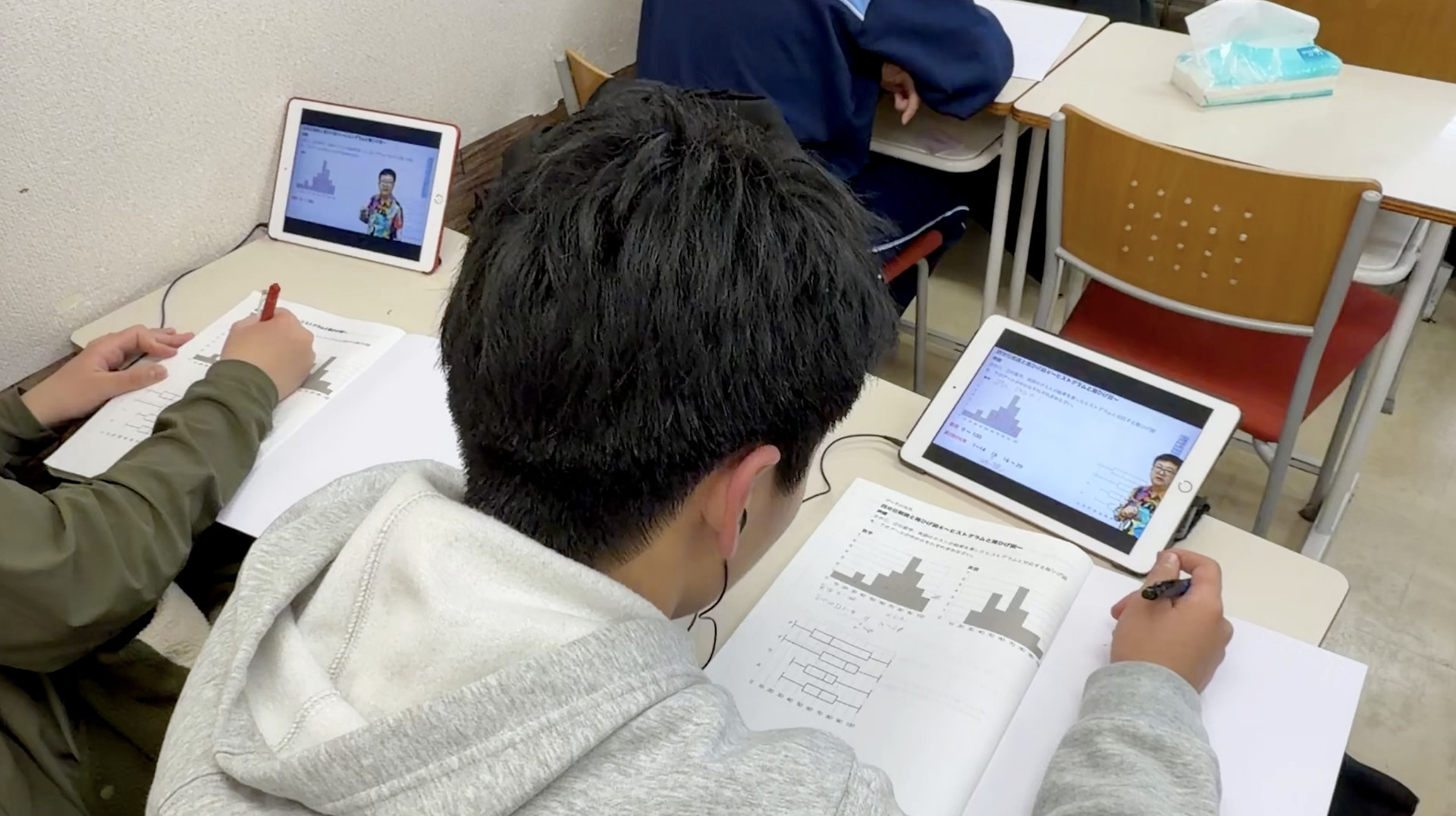 タブレットの授業を見ながら、手元の教材に取り組む中学生。