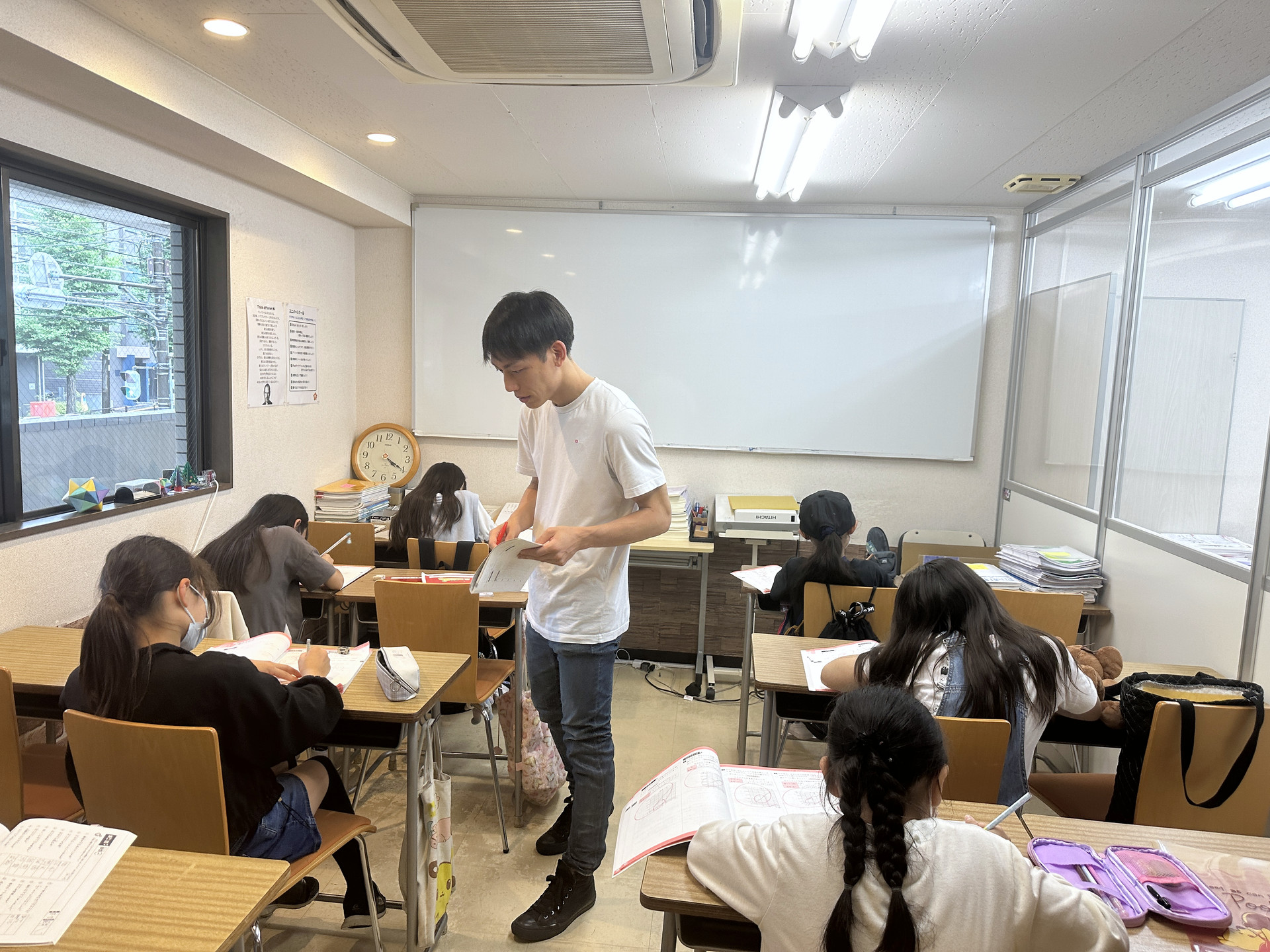 小学部で教材を手に生徒の机を回る先生と、演習に取り組む小学生
